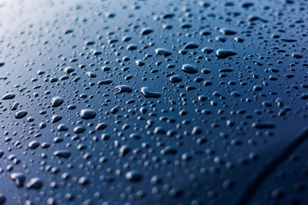 Abstract rain or water drops different size on a blue car hood surface with shiny reflections. Wate